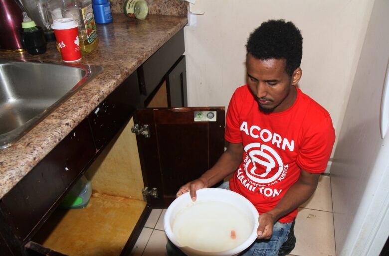 Man holds bowl of water in kitchen near sink.