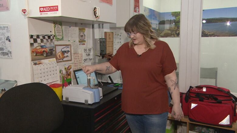 A woman wearing a red shirt can be seen touching a machine that tests drugs for contamination. 