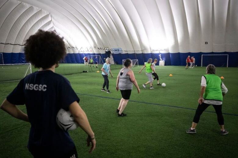 People play soccer under a white dome, on a green turf field.