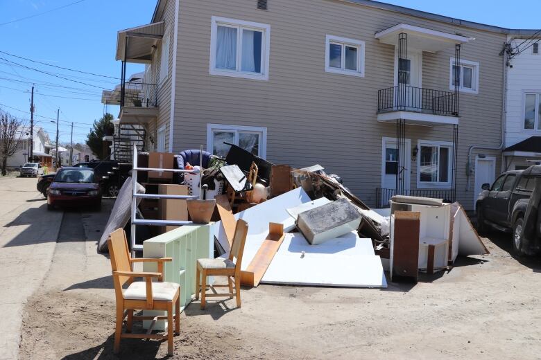 A pile of damp and destroyed furniture laid out near a series of houses. 