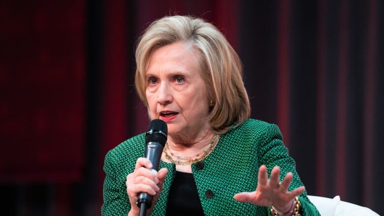 Former U.S. Secretary of State Hillary Clinton speaks to a crowd in Ottawa. She's wearing a green blazer and is holding a microphone.