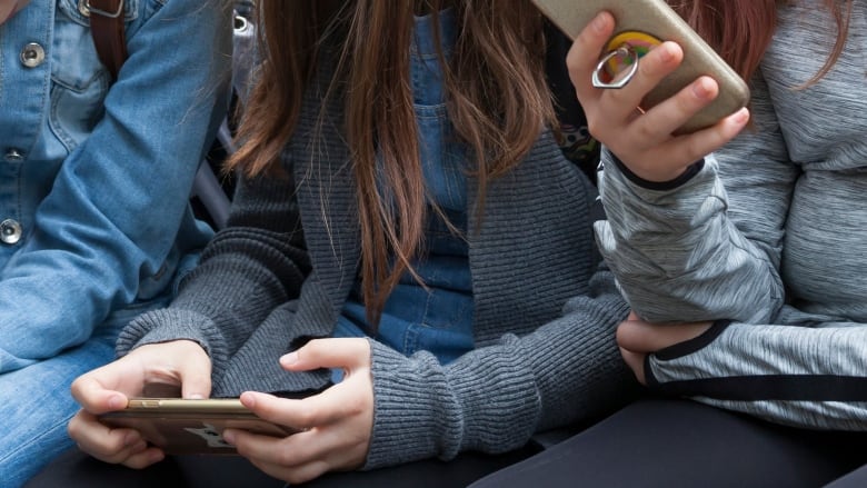 Three girls use cellphones in a stock image.