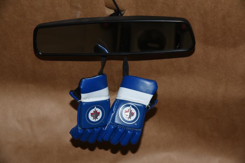 A small ornament depicting hockey gloves with the Winnipeg Jets logo hangs on a car's rear-view mirror.