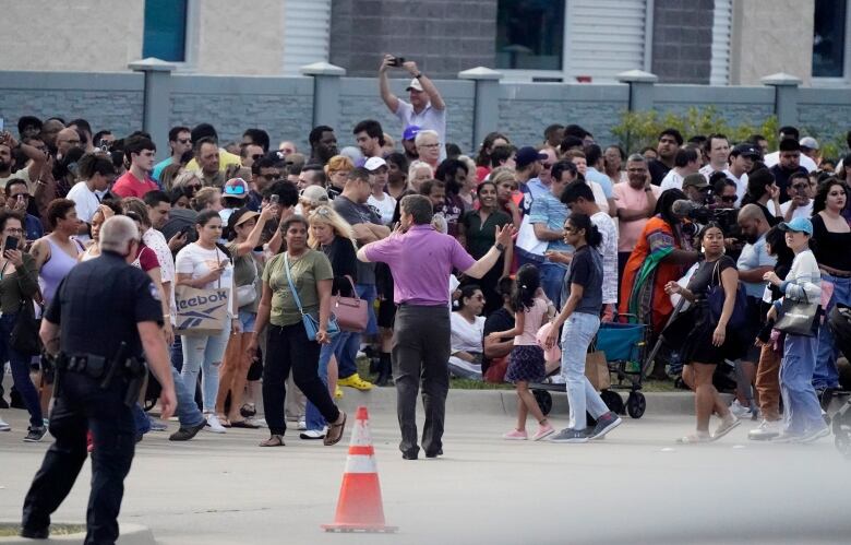 A crowd of people gather as a person tries to direct them.