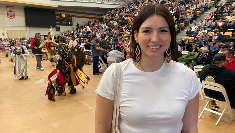 A woman is pictured smiling to the camera in front of a powwow.