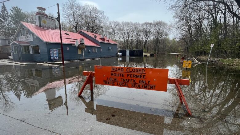 A flooded roadway blocked off with a sign saying 