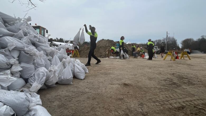 A person throws a bag filled with sand onto a large pile of sandbags. 