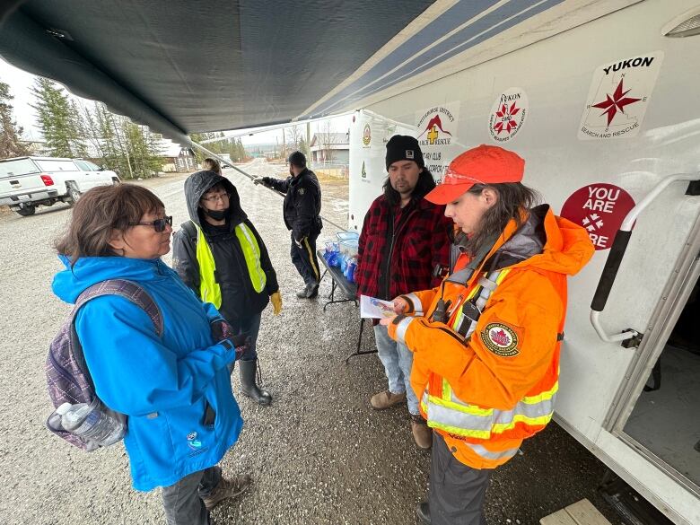 The photo shows a group of three people listening to a Search and Rescue officer, who's holding a map. 