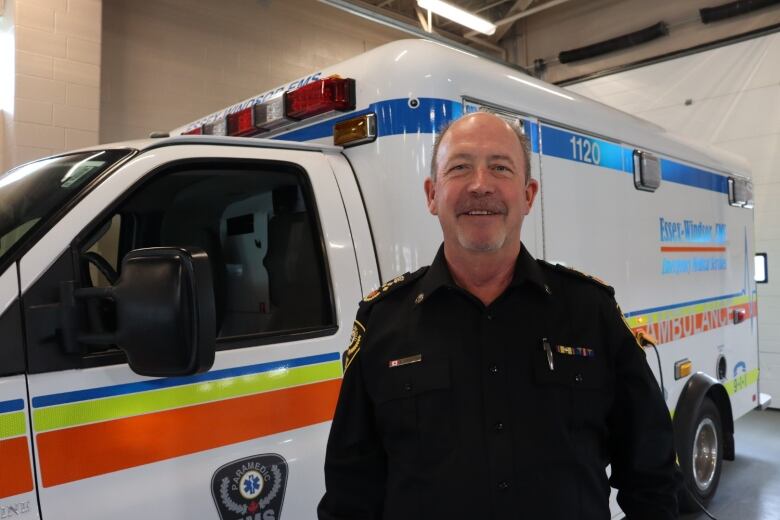 A man wearing a uniform stands by the front end of an ambulance.