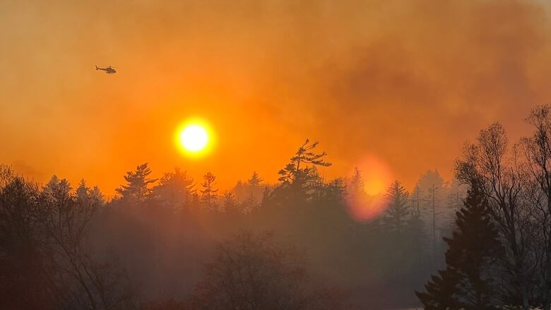 Helicopter flying over smoky fire and sun bright setting sun