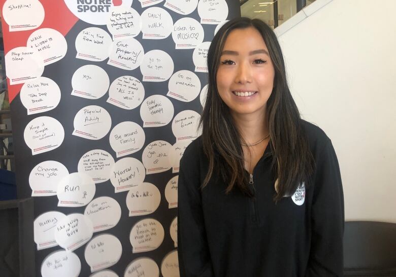 A young woman with long, dark hair poses next to a tall poster covered in speech bubbles that have words written on them.