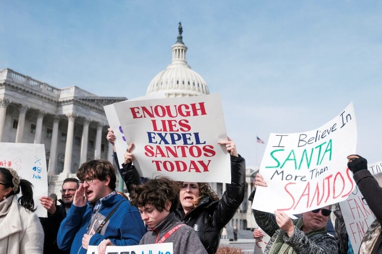 Several people are shown holding signs in a demonstration on the steps of the U.S. Capitol building.