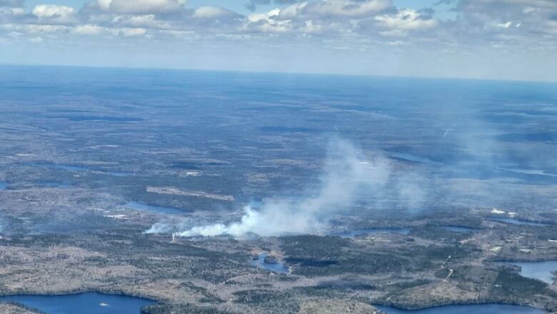 An aerial shot shows a plume of smoke rising from the forest, with the horizon in the background.