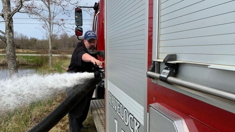 A man stands next to a red fire truck as water shoots out from an opening in the side.  