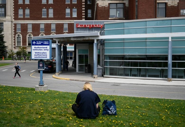 A person rests on a lawn outside a hospital.