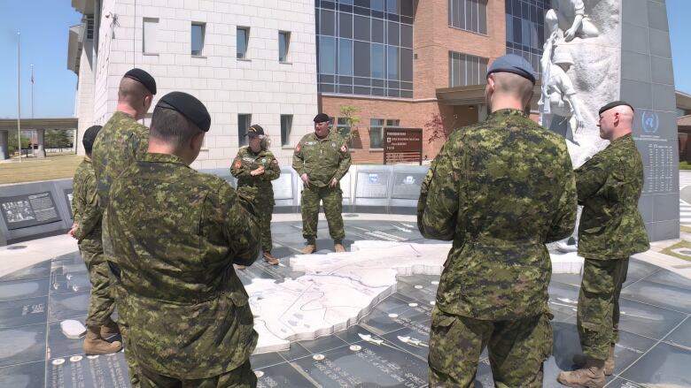 Soldiers stand around a memorial that includes a stone map of the Korean peninsula and two soldiers rising from it.