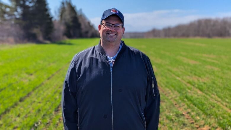 A man stands in a field with visibly green winter wheat growing 