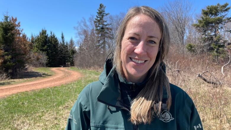 Hailey Paynter a landscape ecologist with Parks Canada smiles for a photo. Her blonde hair is tied in a low pony tail and she is wearing a green Parks Canada jacket. 