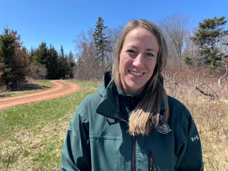 Hailey Paynter a landscape ecologist with Parks Canada smiles for a photo. Her blonde hair is tied in a low pony tail and she is wearing a green Parks Canada jacket. 