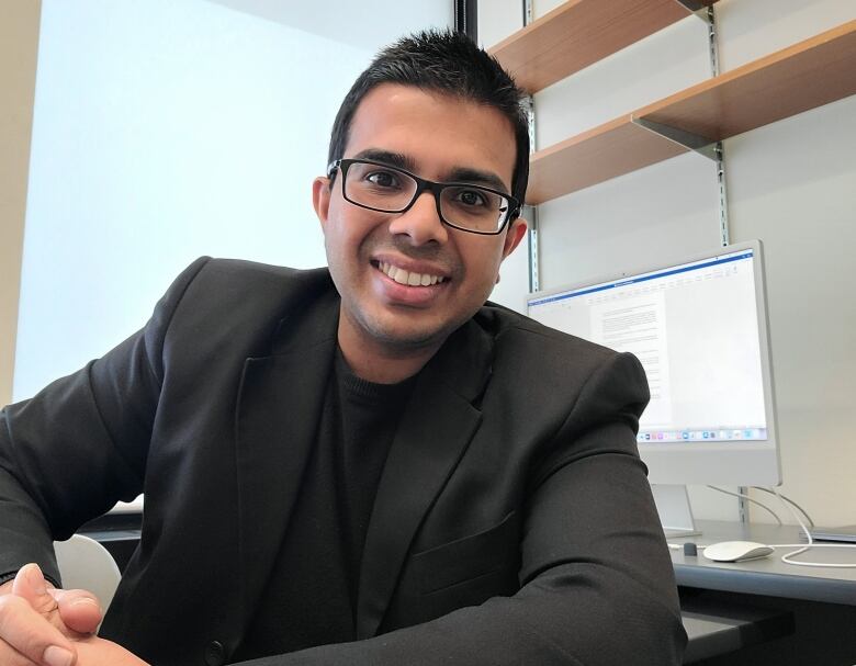 A man sits smiling at his desk