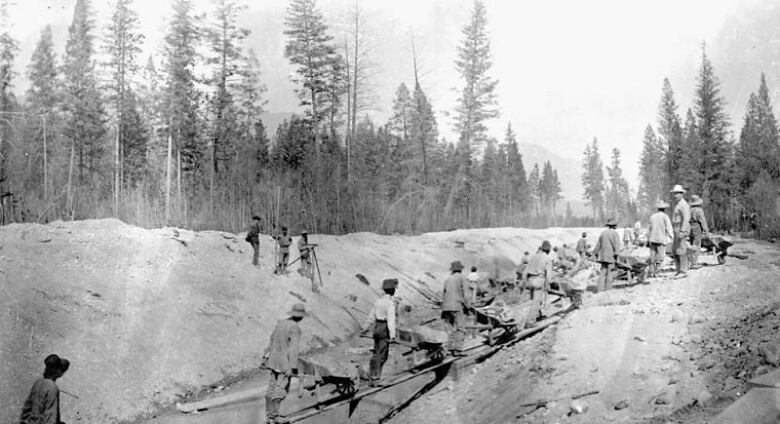 A line of men working along a track with mountains and trees around.