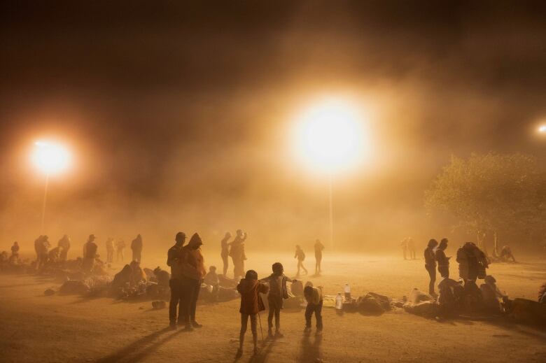 People gather in dim orange light by the border waiting for Title 42 to lift.