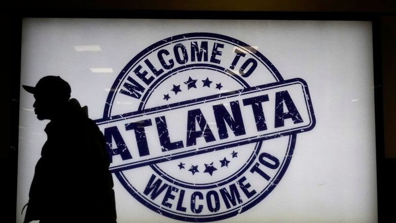 A traveller waits to board a flight at Hartsfield-Jackson Atlanta International Airport in Atlanta. They are standing in front of a sign that says, 