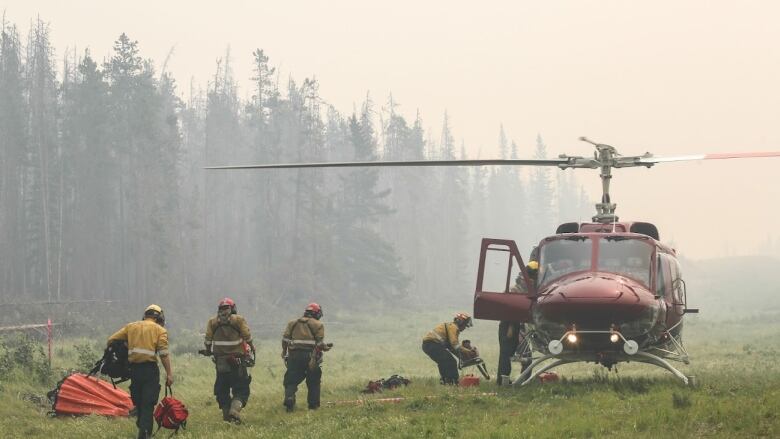 Firefighters in yellow board a red helicopter. There is smoke in the air. 