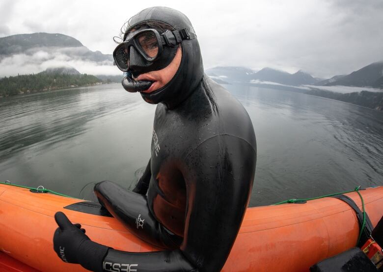 A man in scuba gear sits on a boat, looking back at the camera.