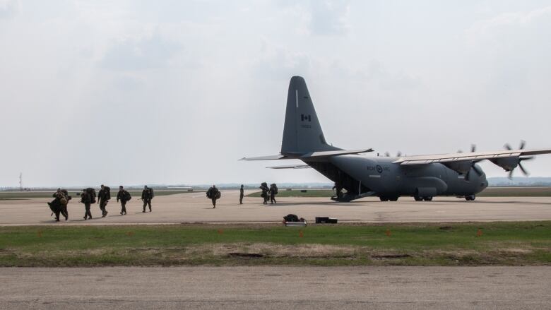 Soldiers in green uniforms board a plane.