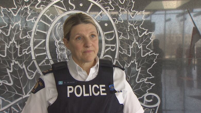 A woman with pulled-back blonde hair wears a police vest. 