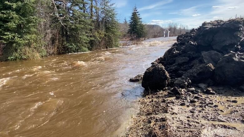 A rushing river is seen with rocks piled on the bank.