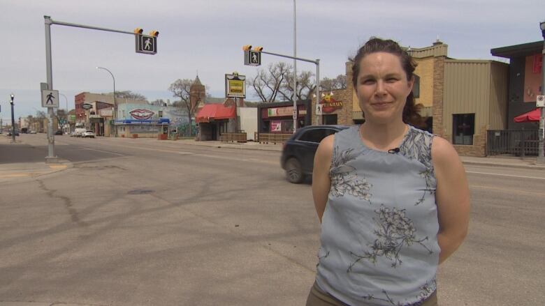 A woman is standing in front of a street, with a crosswalk visible in the background.