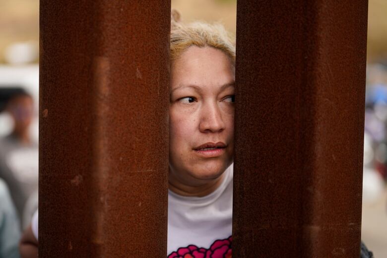 A woman peers through a space in a wall.