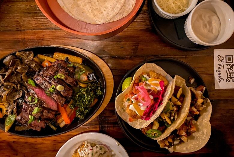 Tacos and fajita ingredients sit on different plates on a table top.