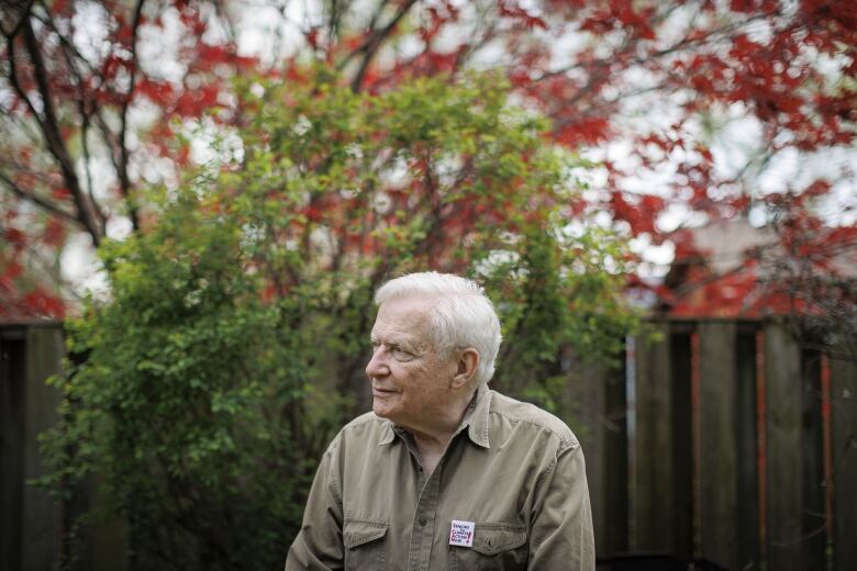 An elderly man is seen side-profile in his backyard.