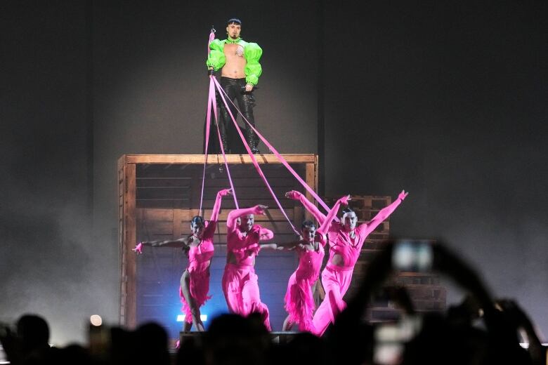 A singer on a platform holds leashes connected to dancers below them during a performace.