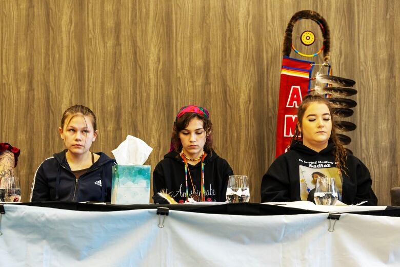 Three women sit behind a table at a news conference. 