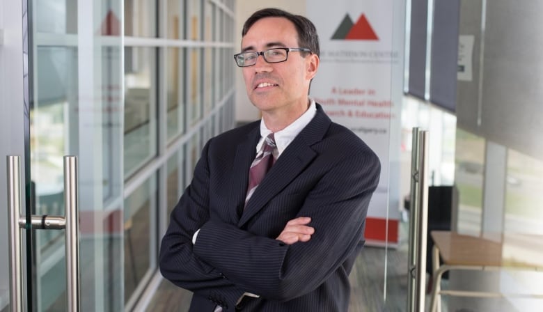 Dr. Paul Arnold is wearing glasses and standing with his arms crossed in a hallway with windows along one side.