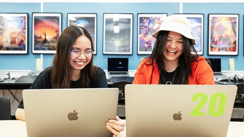 two students sit in their classroom going over their work and laughing. 