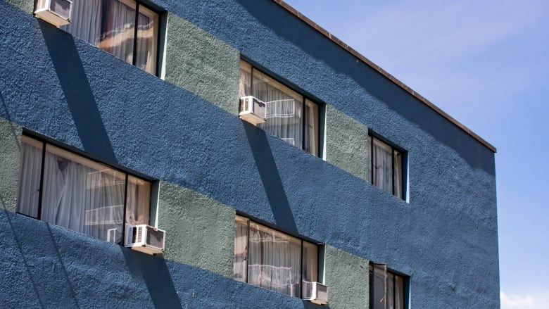 A blue low-rise apartment building in Vancouver's West End has multiple air conditioners hanging out its windows.