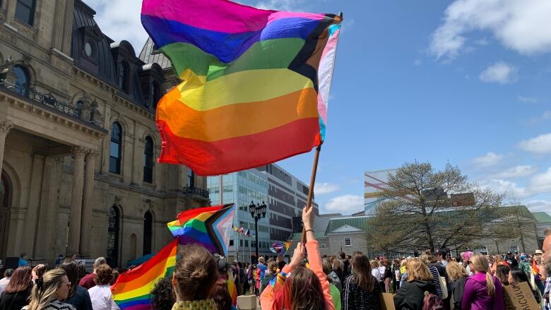 A group of people stand outside a historical building waving pride flags.