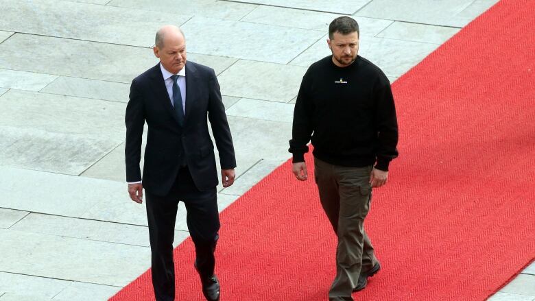 Two men walk on a red carpet.