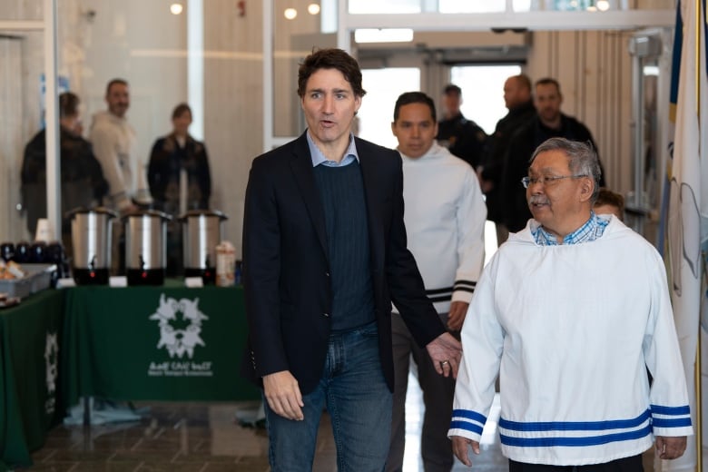 Two men walking down a hallway with a group of people behind them. 