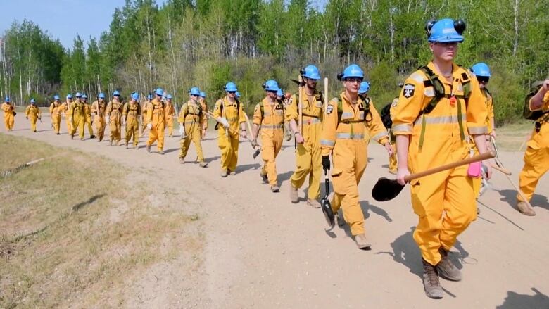 People dressed in yellow overalls march on a dirt road.