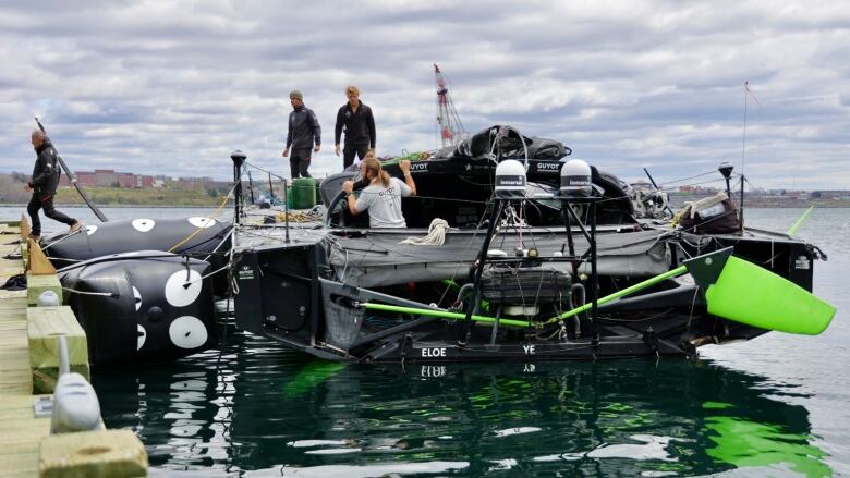 Three team members are on the boat docked in the Harbour while a fourth member walks off the boat onto the dock. 