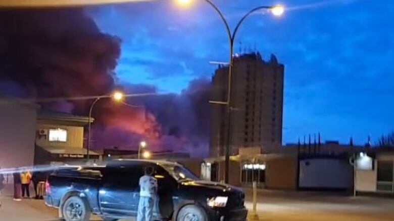 Black smoke rolls into the sky above an urban skyline.