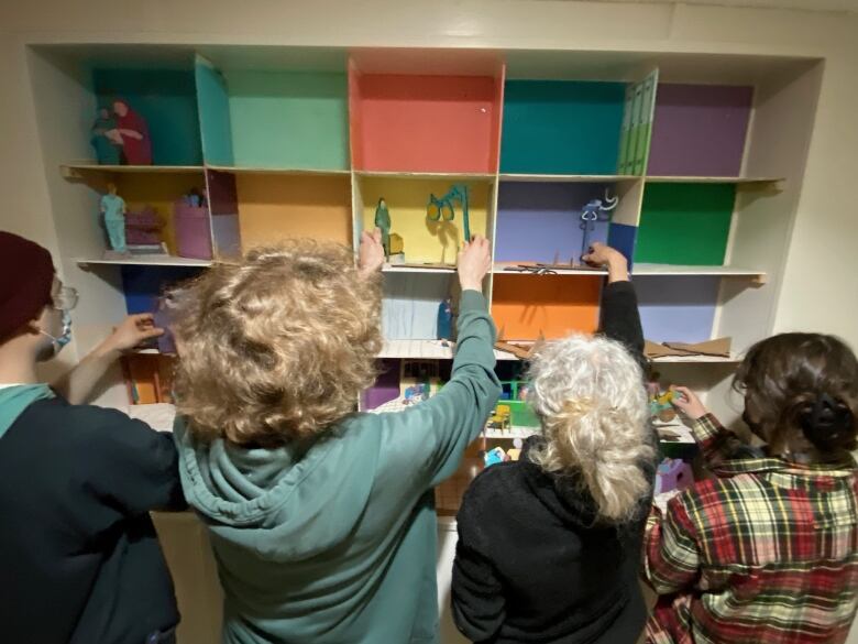 Four people add paper cutouts to colourful boxes inside a wall. 