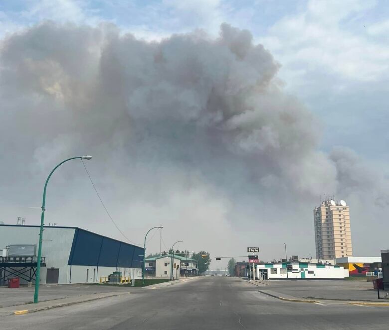 A plume of smoke is seen rising behind some distant city buildings.