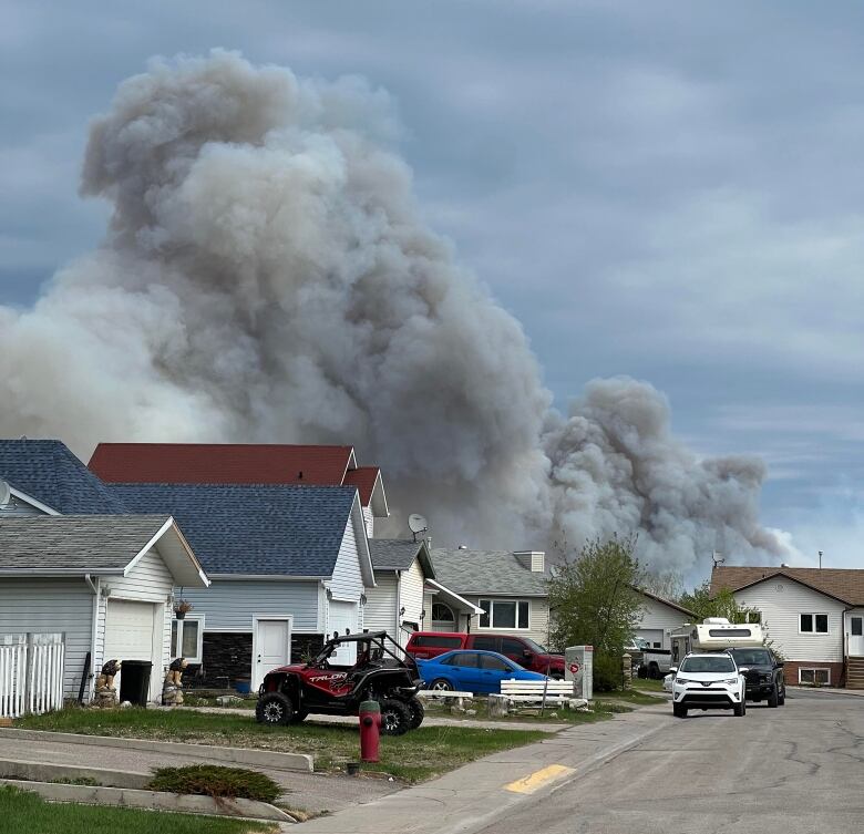 A plume of smoke is seen rising behind some homes on a residential street. 